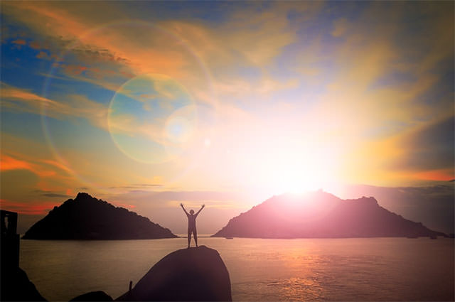 Man-With-Arms-Up-And-Sunset-Behind-Island